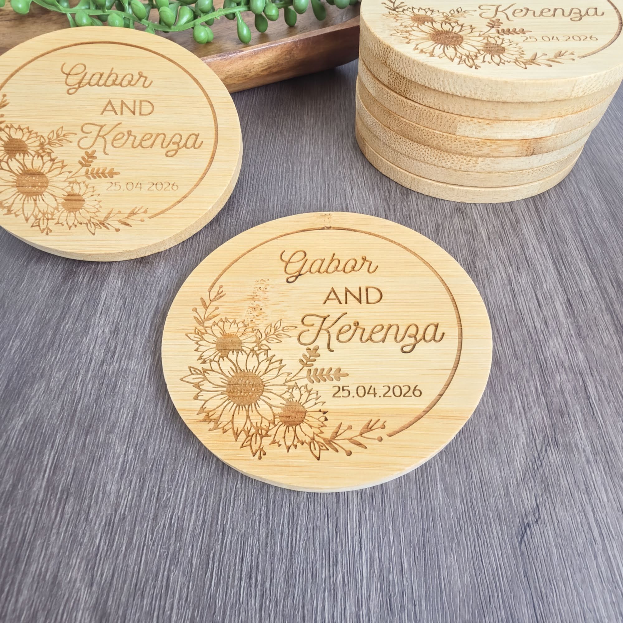 a set of wooden coasters with the names "Gabor AND Kerenga" engraved on them. The coasters are placed on a wooden surface, and there are additional coasters stacked nearby.