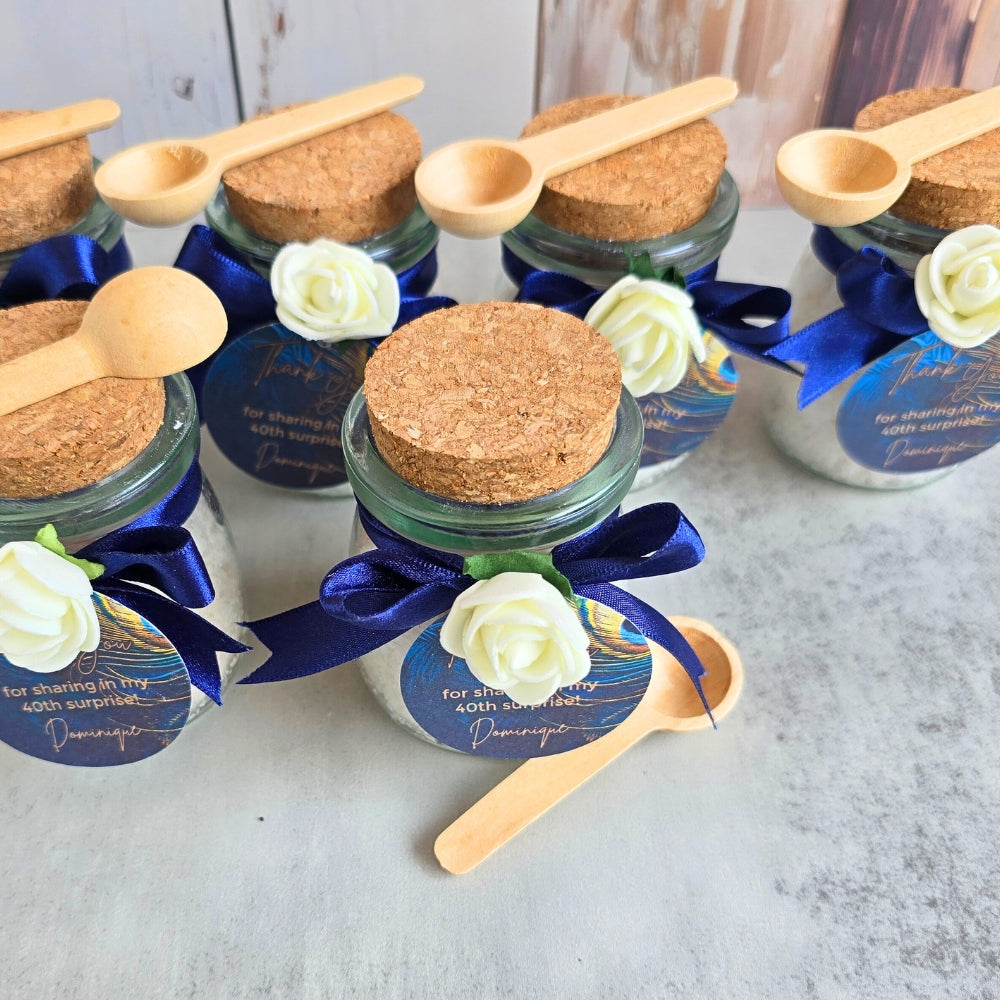 Small jars with cork lids, wooden spoons, white flowers, and blue ribbons filled with bath salts and used to give as favours