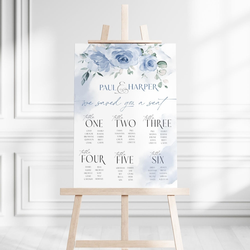 Wedding seating chart with blue floral design on a white background, displayed on a wooden easel.