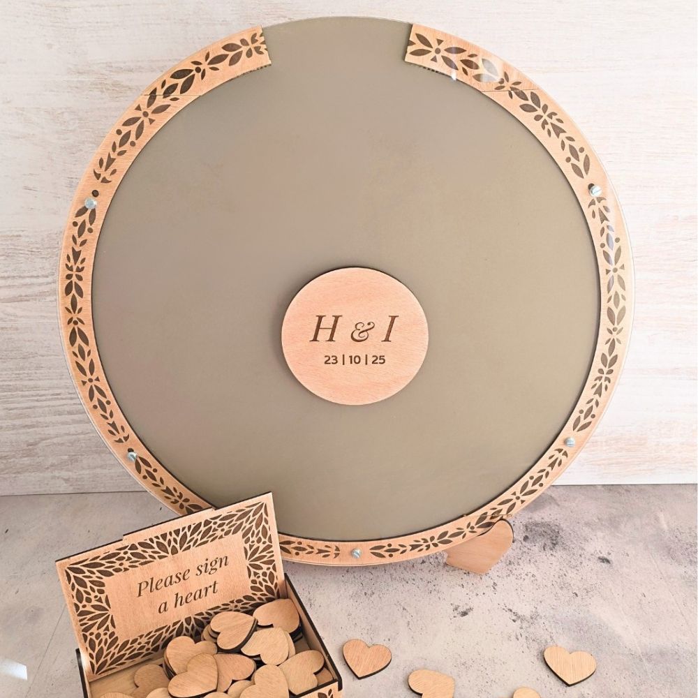 Round wooden dropboaxx with laser-cut edge and 'H & I' engraving, accompanied by heart-shaped wooden pieces.
