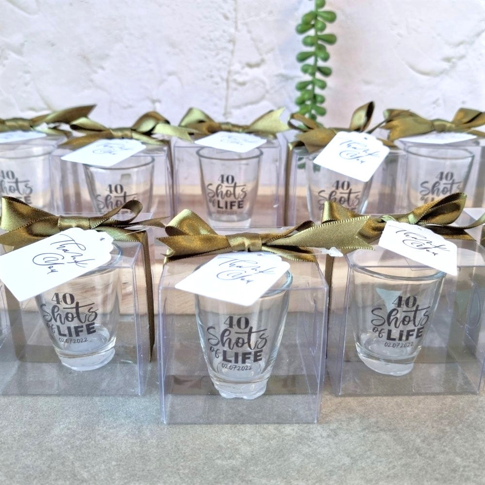 Set of shot glasses with '40 shots of life' text in clear packaging with gold ribbons.