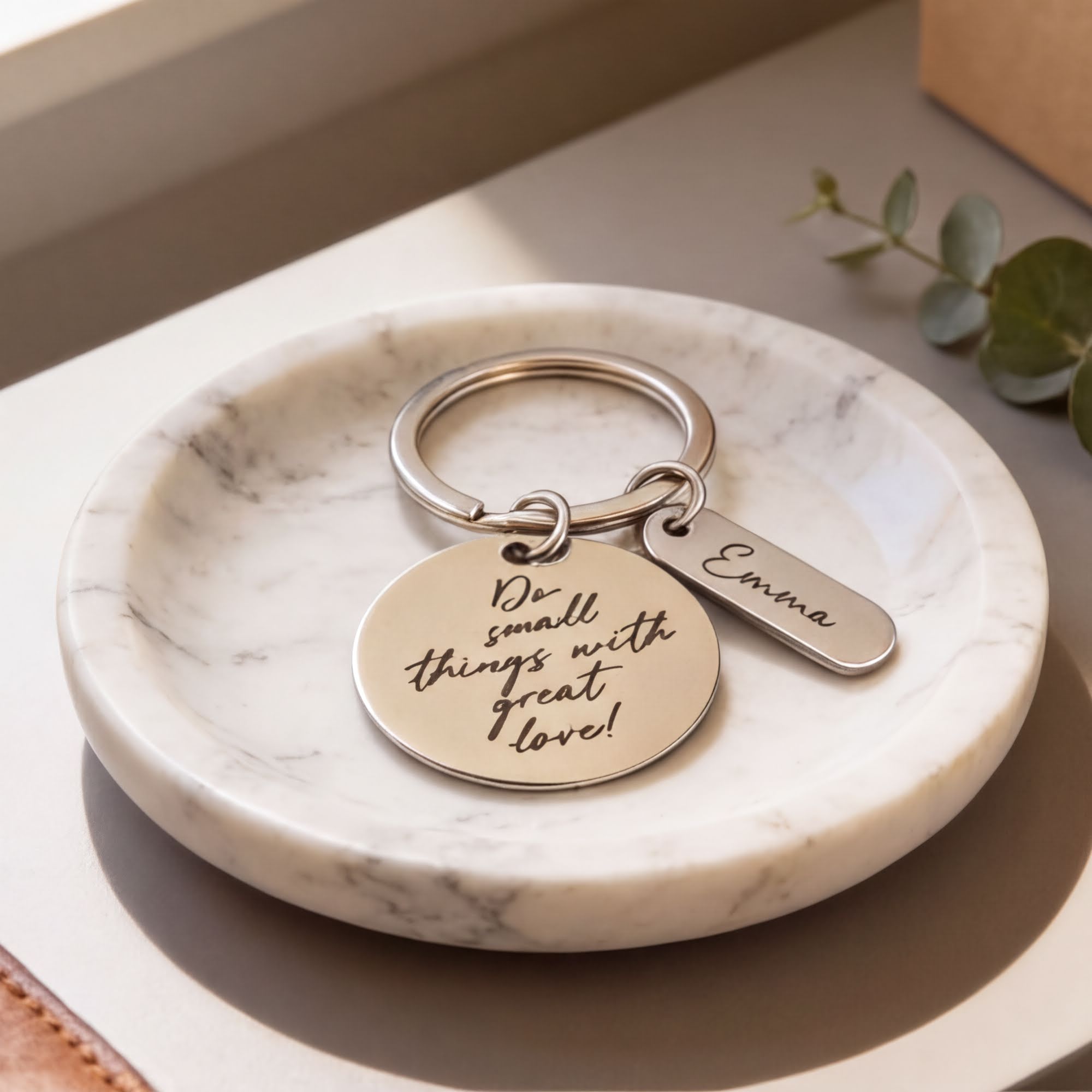 A keychain with a round metal charm and a small metal tag attached to it, placed on a white marble surface.