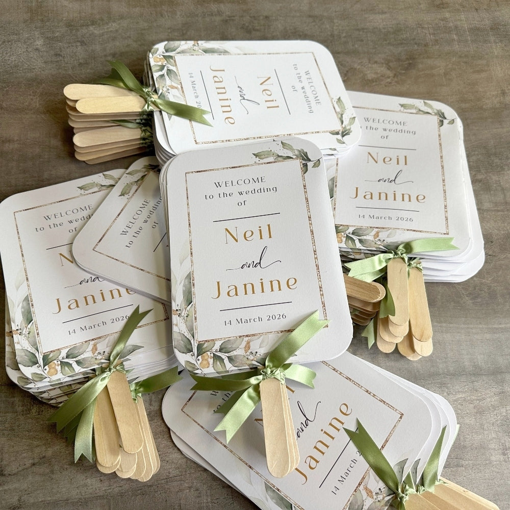 several white wedding invitations with gold and green accents, arranged on a wooden surface. The invitations feature the names "Neil and Janine" and the date "14 March 2020".
