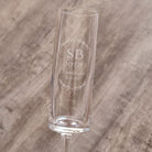 A clear glass with the inscription "SB 10th ANNIVERSARY 2.05.2026" engraved on it, standing on a wooden surface.