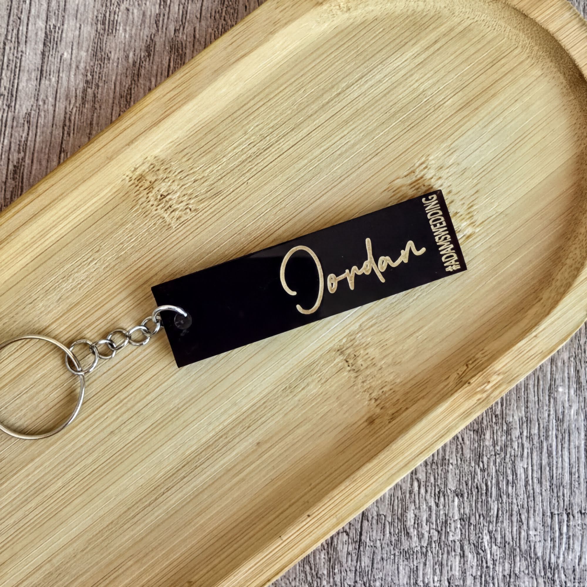 A black rectangular keychain with the name "Jordon" engraved on it, resting on a wooden surface.