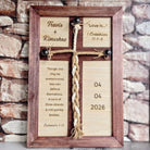 A wooden cross with a religious inscription and a date displayed on it, placed against a brick wall background.