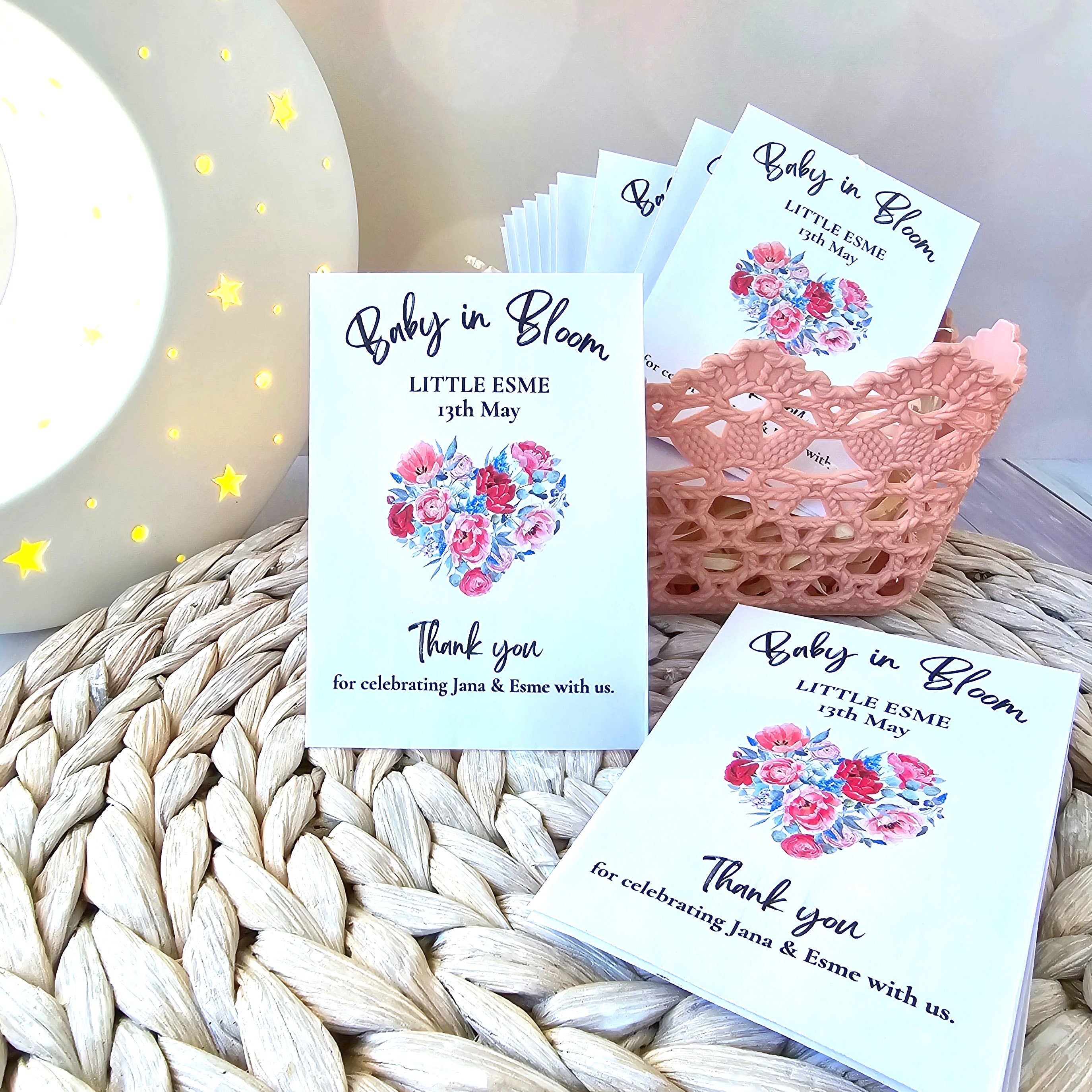 Baby shower thank you favour seed envelopes with floral designs on a woven surface.