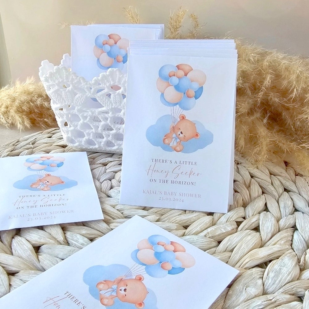 Baby shower seed pack favours with teddy bear and balloons design on a textured surface.