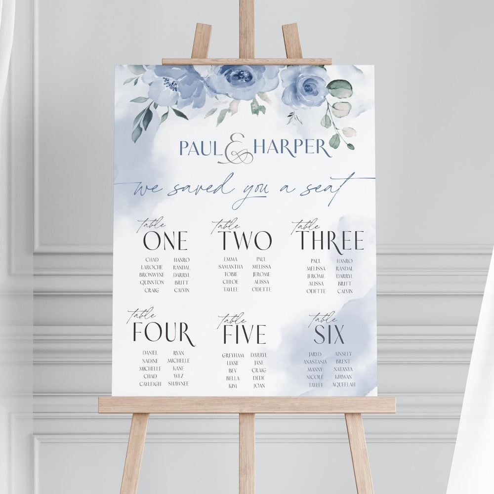 Wedding seating chart with floral design on an easel against a gray wall.