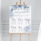 Wedding seating chart with floral design on an easel against a gray wall.