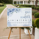 Wedding welcome sign with floral design and names on an easel outdoors.