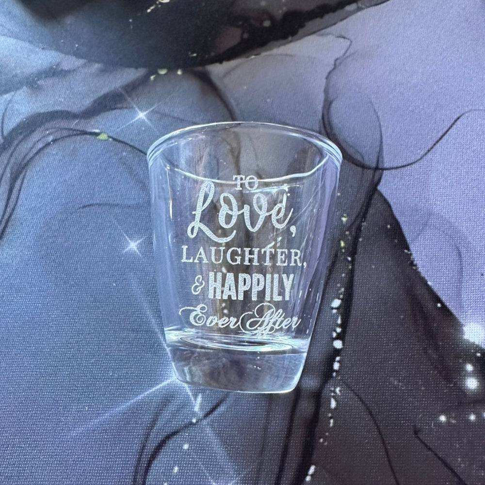 A clear shot glass with personalized engraved text 'To Love, Laughter & Happily Ever After' wedding favour