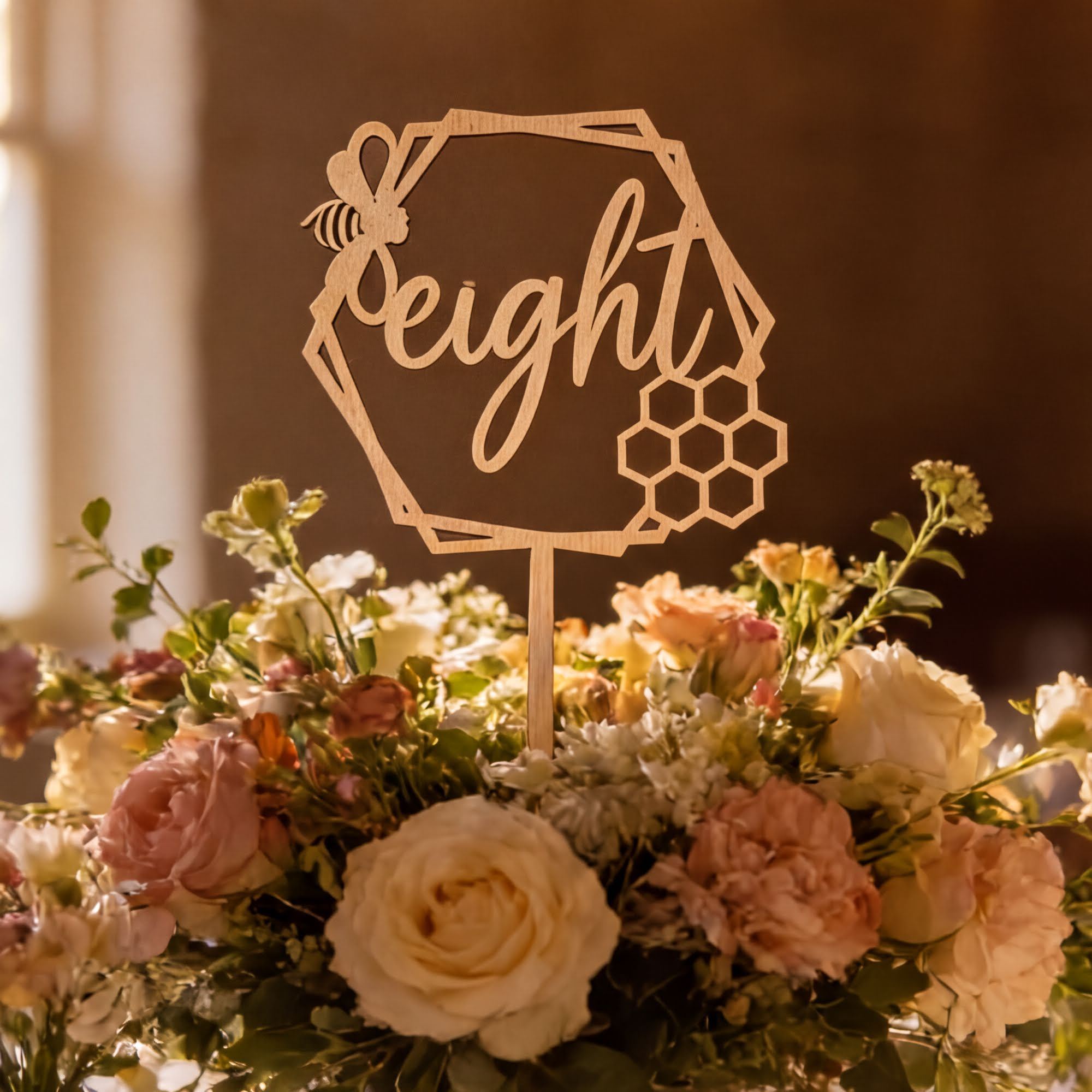 A wooden hexagonal cake topper with the word "eight" written on it, surrounded by a floral arrangement of various flowers.
