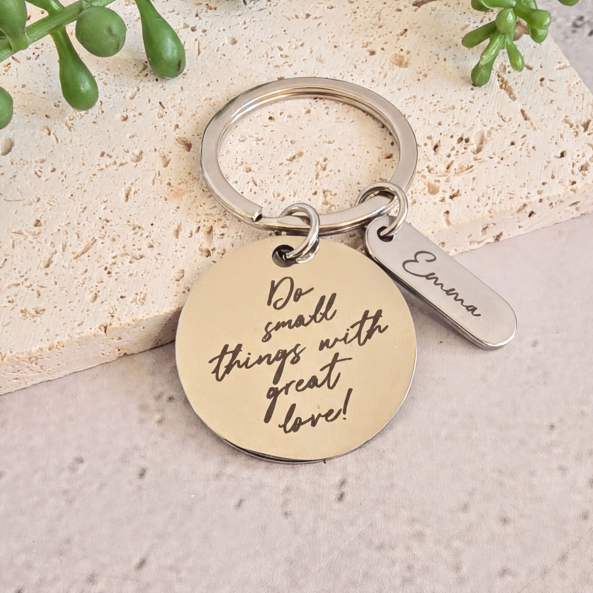 A keychain with a round metal tag and a small metal charm attached to it, featuring a motivational quote.