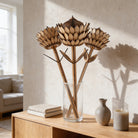 a wooden vase with three wooden flowers, a stack of books, a candle, and a small vase on a wooden table.