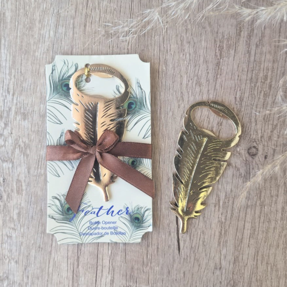 Gold feather opener tied onto a card that is decorated with peacock feather print, tied down with a brown satin ribbon which is tied into a bow.