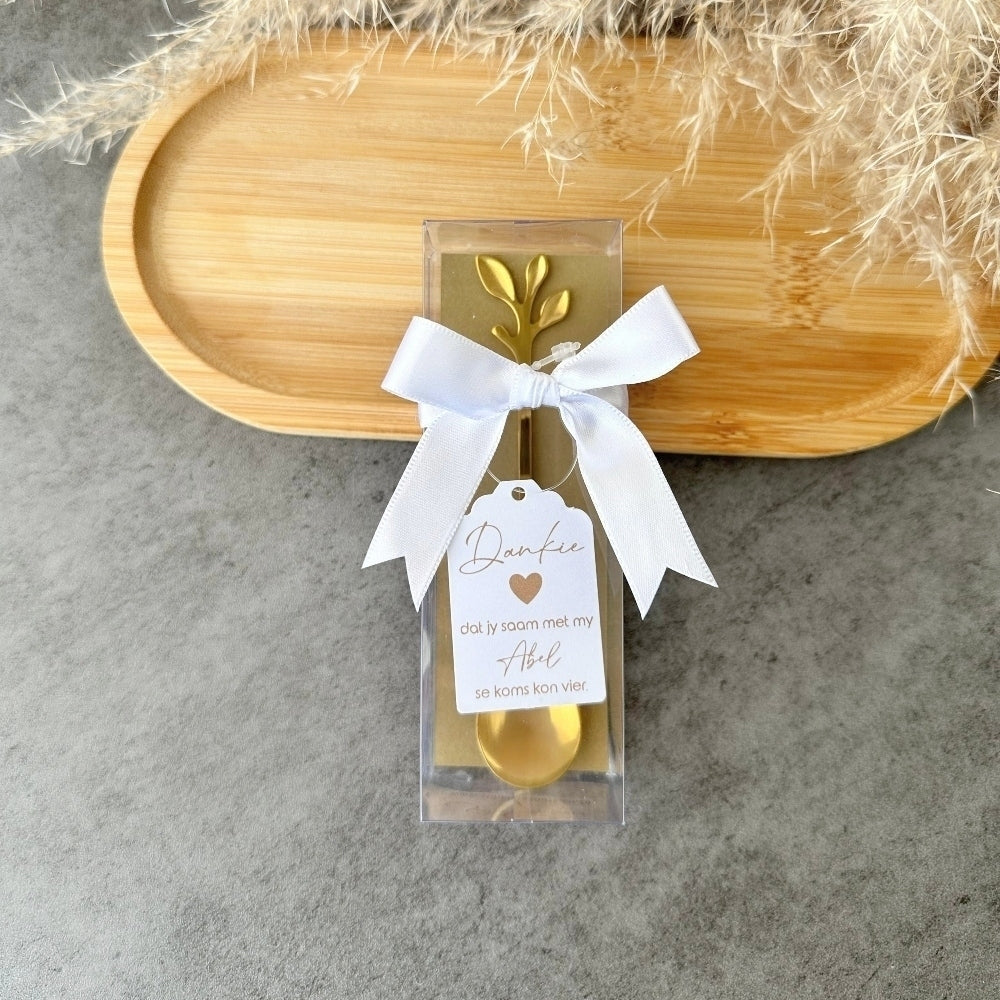 Gold spoon in a clear package with a white ribbon and tag