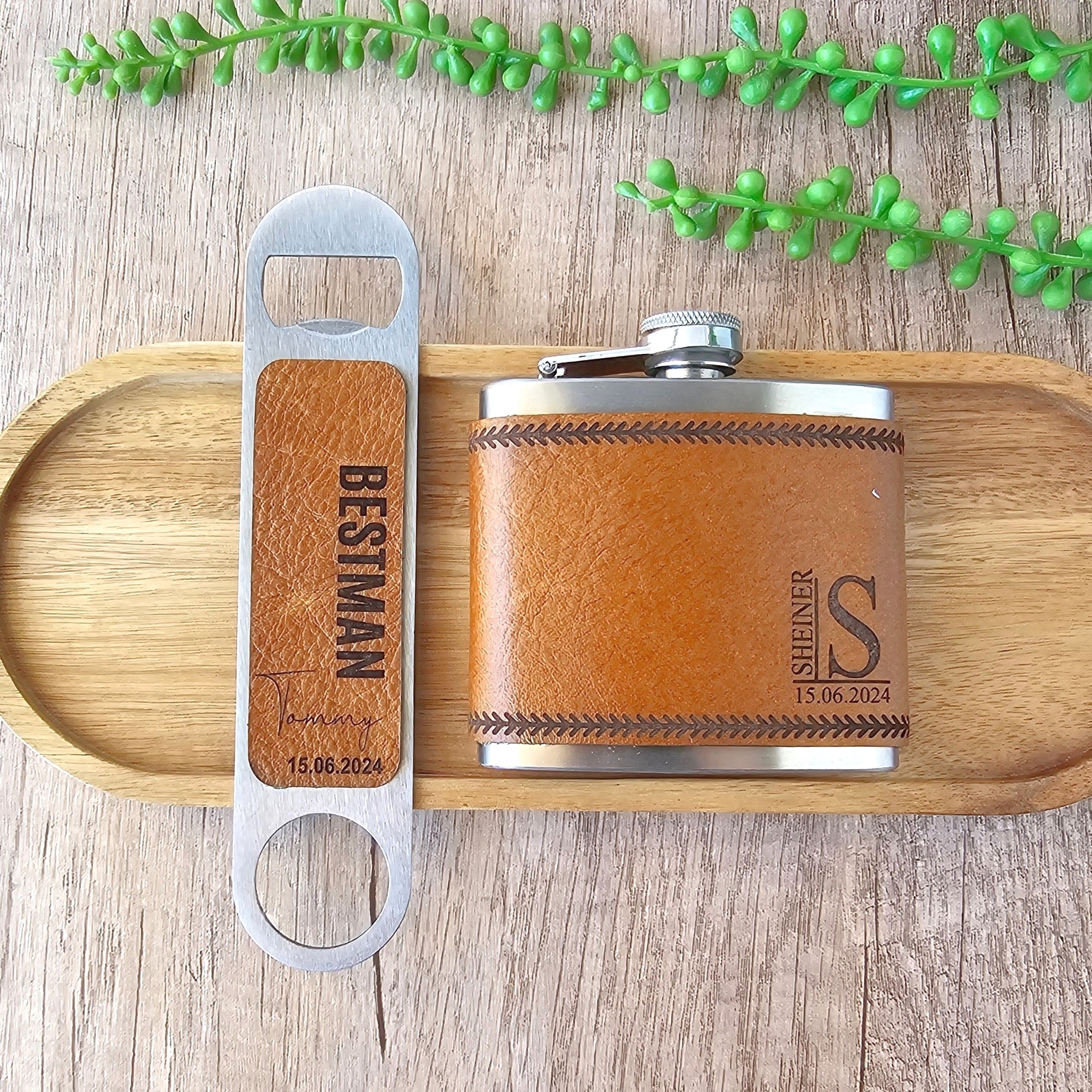 Brown leather flask and wooden bottle opener with engraved text on a wooden tray.